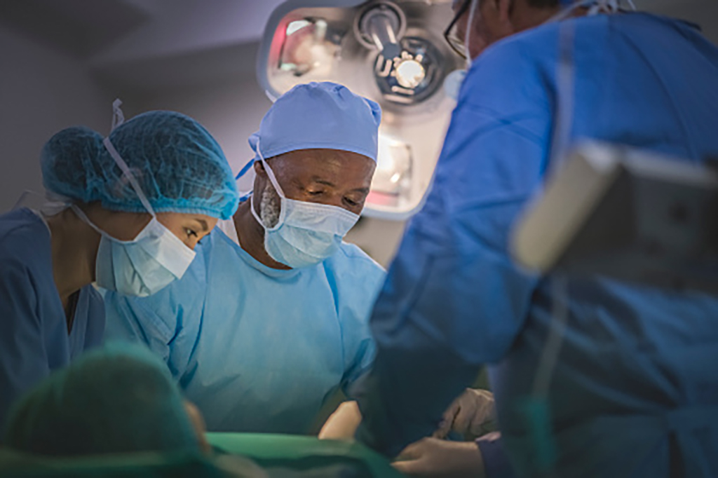 A group of three surgeons performing surgery on patient in operating room