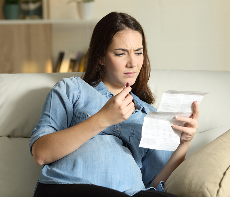 A confused pregnant woman reading a leaflet before take a pill