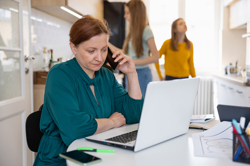 Woman sitting at the table at home and doing business, using laptop and mobile phone