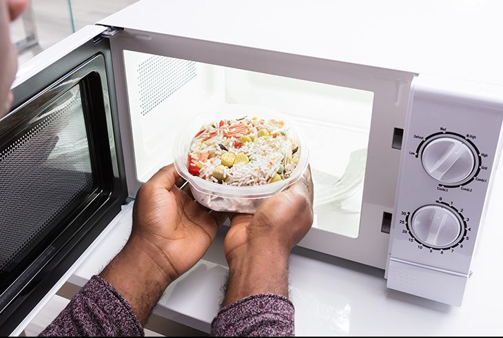 A Man handling heated Food In Microwave oven