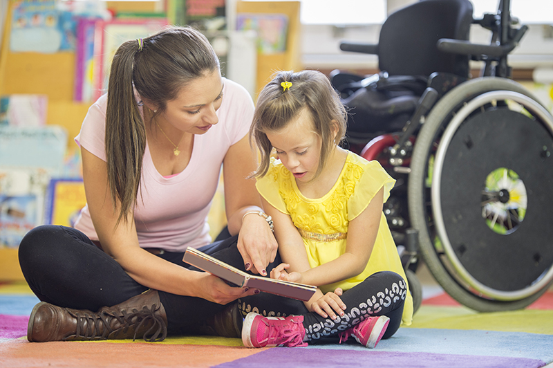 Woman and child looking at a book. There is a wheelchair in the background.