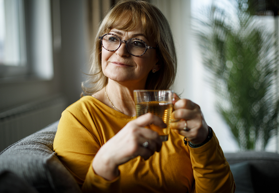 A smiling senior woman sitting on sofa and drinking tea at home