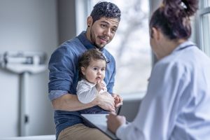 A doctor talking to a father who is holding their baby