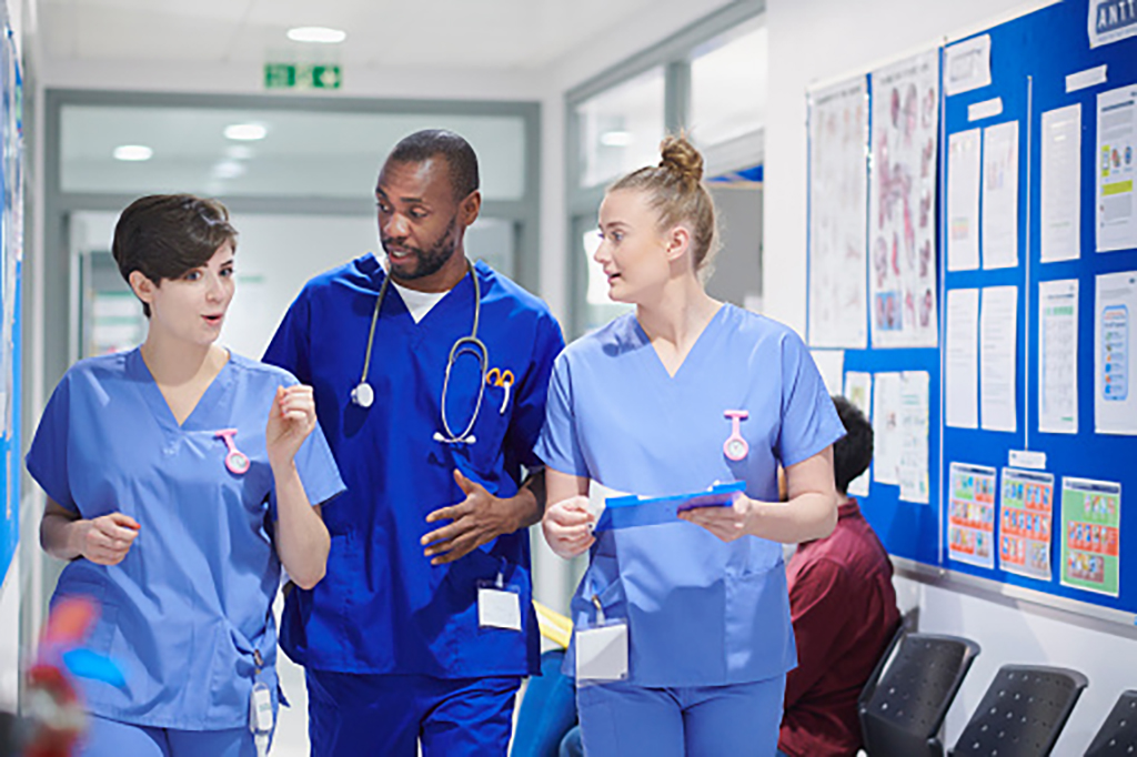 A medical consultant with two nurses talk and walk along a hospital corridor
