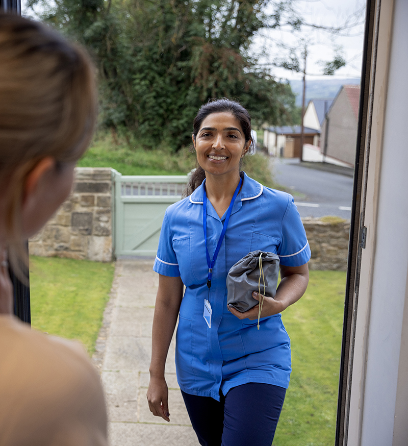 A nurse dressed in her scrubs uniform standing outside a patient's house