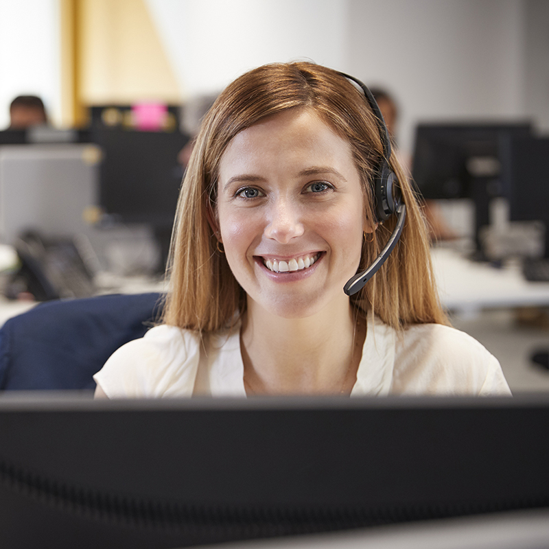 A woman working at computer with headset in busy office