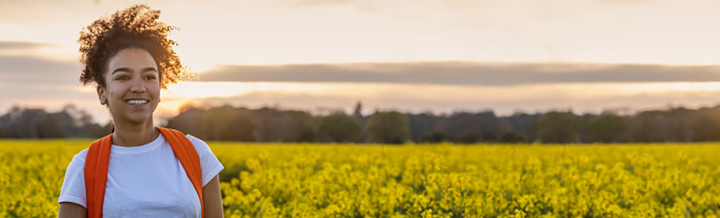 Young woman with a backpack hiking through a field of yellow flowers