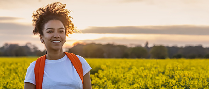 Young woman with a backpack hiking through a field of yellow flowers