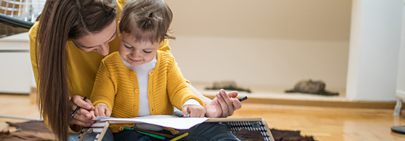 Mother and daughter drawing on a white paper while sitting on the floor