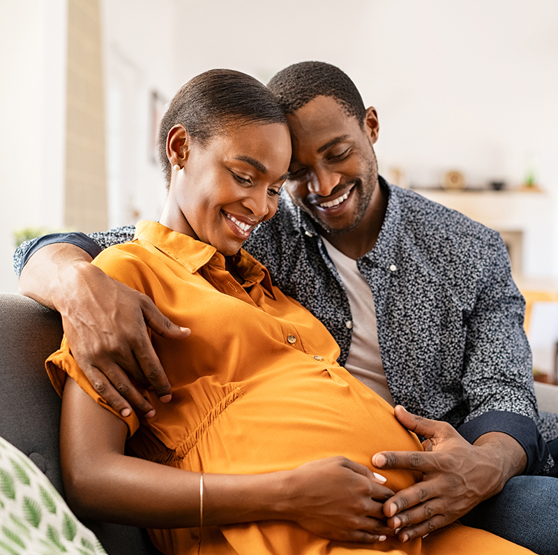 Two expectant parents hugging each other whilst cradling their unborn baby