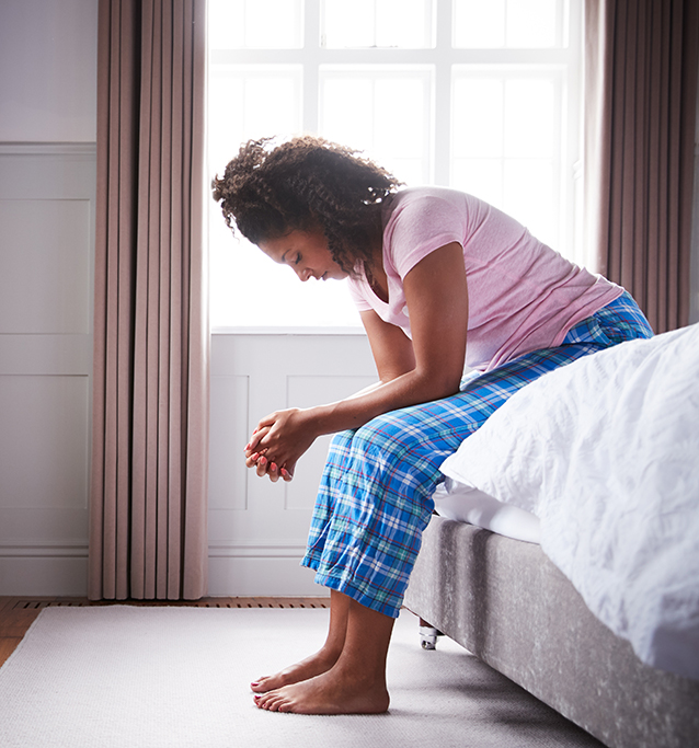 Woman Wearing Pajamas Suffering With Depression Sitting On Bed At Home Woman Wearing Pajamas Suffering With Depression Sitting On Bed At Home