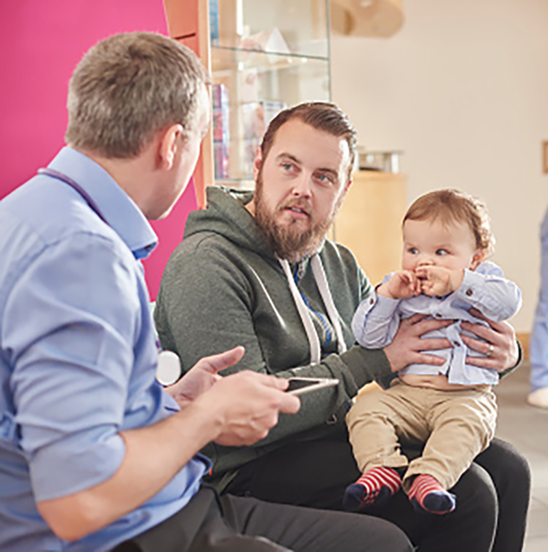 A male doctor talking to his patient and their baby A male doctor talking to his patient and their baby