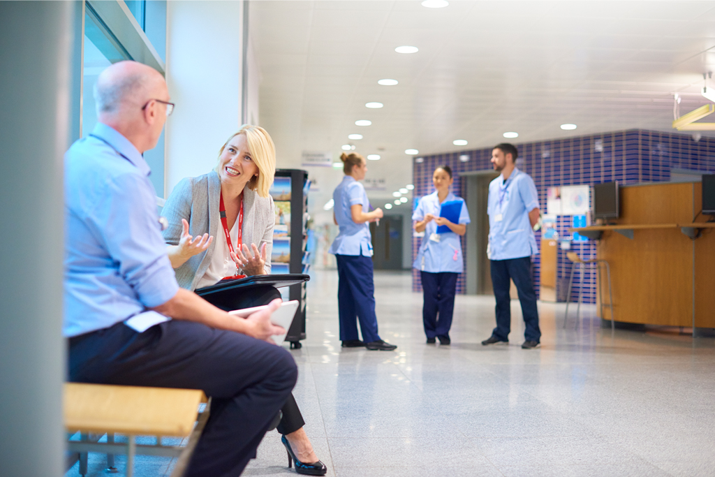 a woman chats to a doctor in a busy hospital corridor