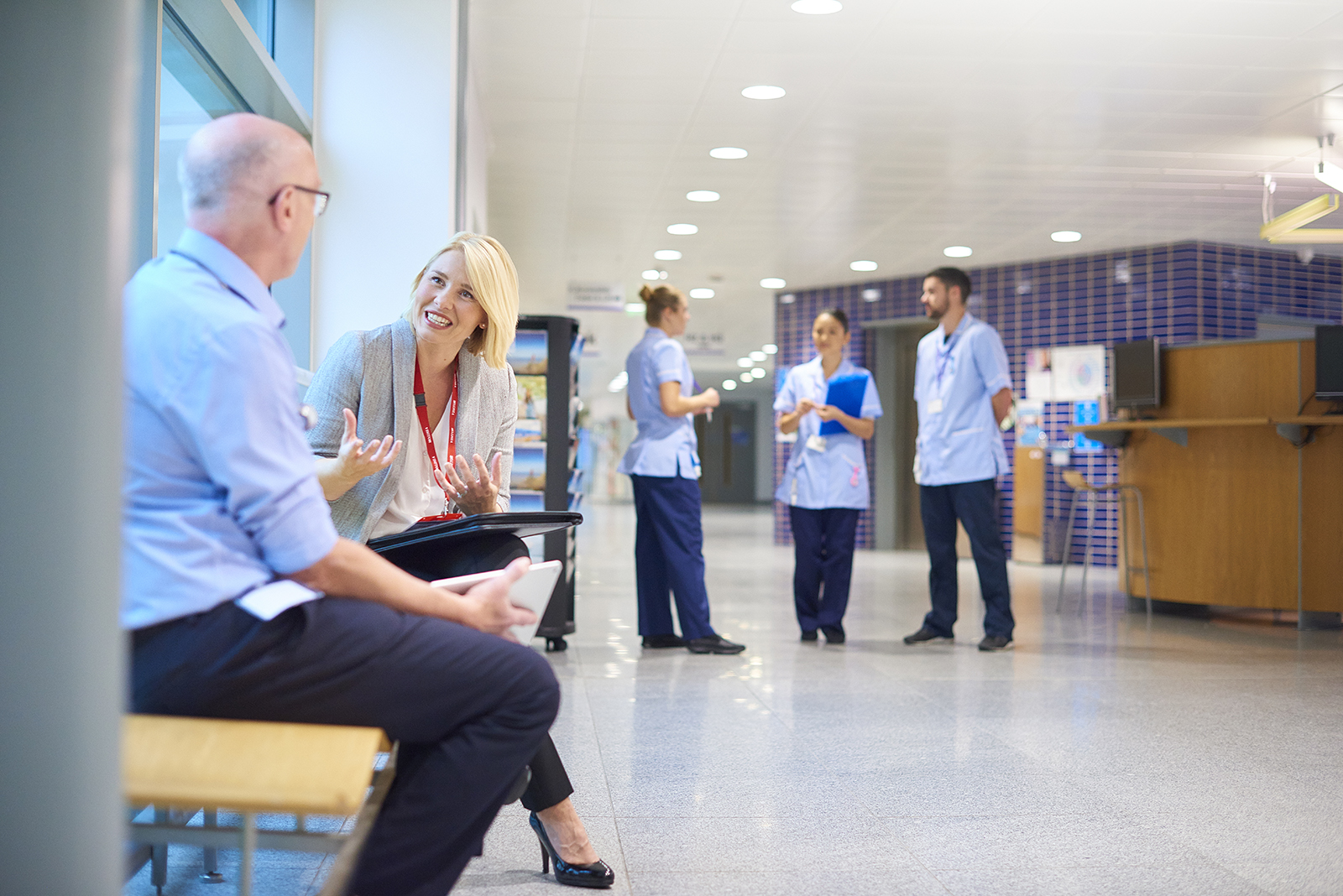 a business woman chats to a doctor in a busy hospital corridor