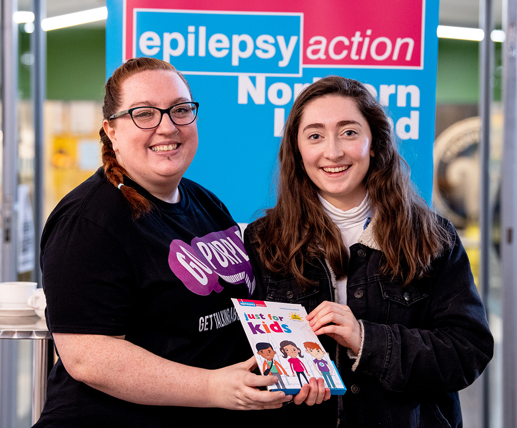 A Epilepsy Action Northern Ireland representative and a young woman holding a just for kids pack