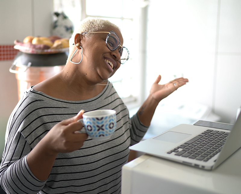 A lady smiling and holding a mug during a laptop based befriending session.