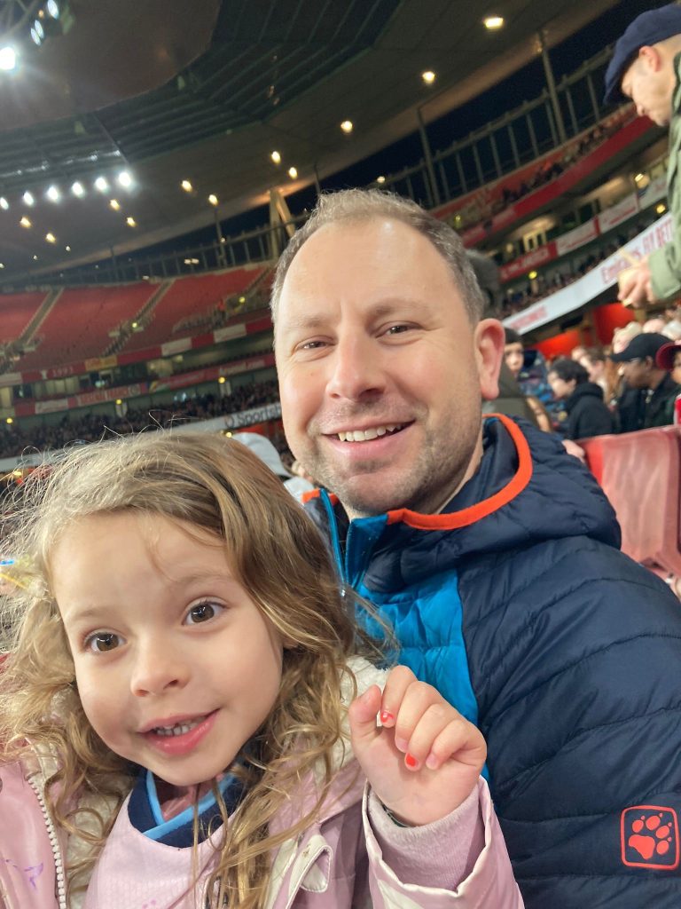 Daisy smiling and waving sat next to her Dad.