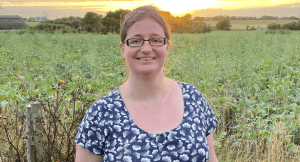 Bec a white woman wearing glasses stands in a field at sunset.