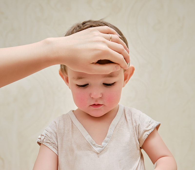 Toddler looking down, an adult hand is on their forehead.