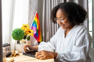 A person looking happy and sitting at a desk with a pride flag