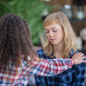 This image depicts a young woman reaching out to help comfort her friend
