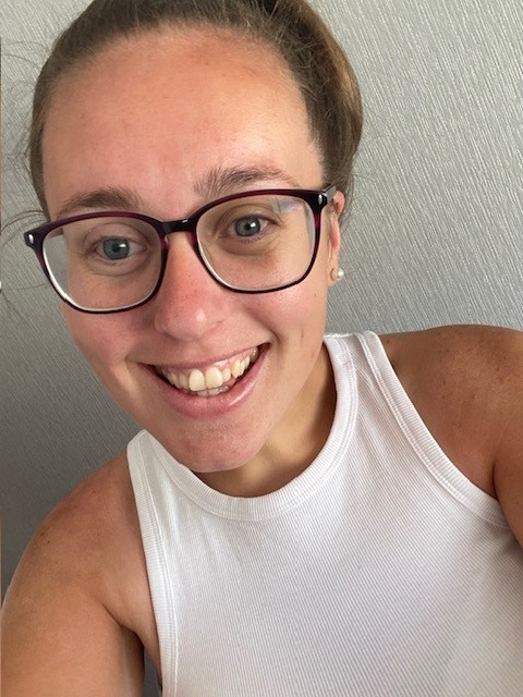 A person smiling, wearing glasses and a white tank top