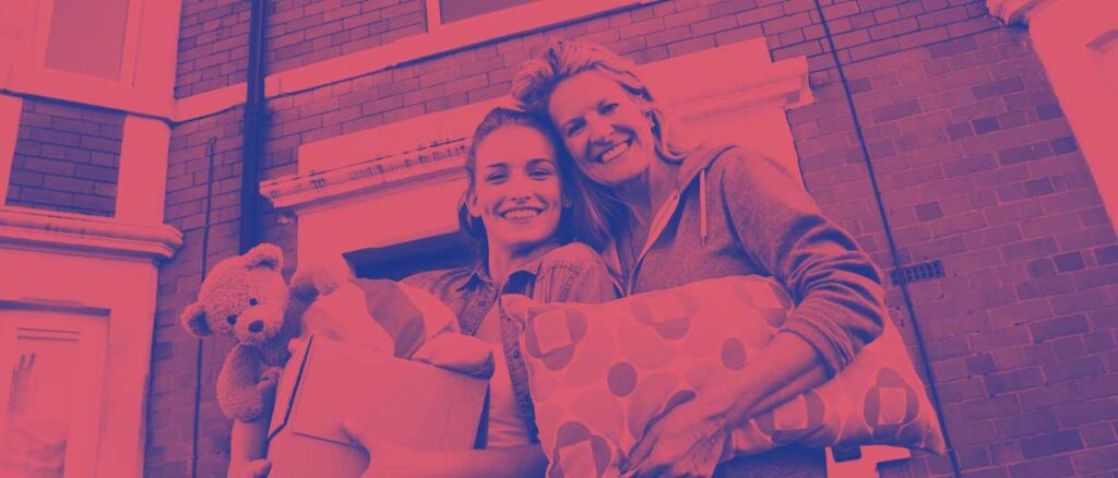 young adult with an older adult holding a pillow, teddy bear and moving boxes