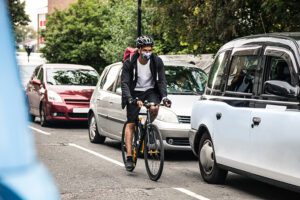 Cyclist commuter among cars with an air pollution mask on