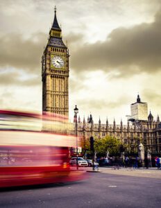 blurry, red double decker bus passing by houses of parliament in UK
