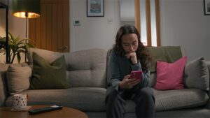 A woman sat on a sofa looking nervously at her phone