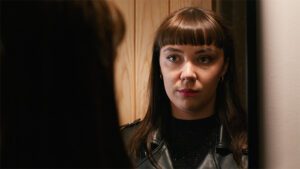A woman looking at herself in the mirror before going out to see her friends, looking serious and a bit worried