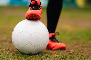 A football on the grass with a female player with one foot on the football and the other next to it