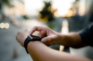 A close up of a young man's hands. He is touching a black smart watch on his wrist to check the information.