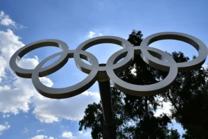 The olympic rings against a blue slightly cloudy sky and a tree
