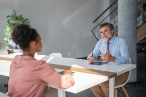 Mature businessman holding eyeglasses and talking with young female employee during a meeting in modern office