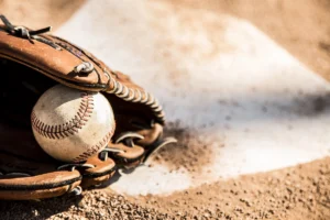 A baseball glove holding a used baseball on home plate of a dirt pitch