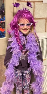 Jessica celebrating purple day with a purple feather boa, pink wig and purple sunglasses