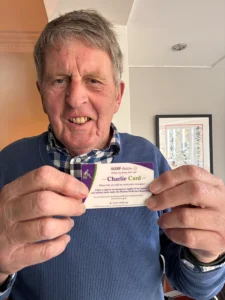 Alan brown in a blue jumper holding up a charlie card