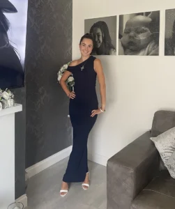 Mia-rose in a blue dress at home, with pictures of her and baby lily on the wall