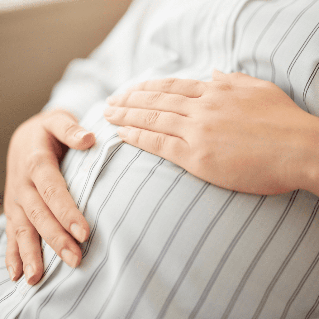 The stomach of a pregnant person in profile, two hands cradle the stomach
