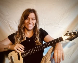 Singer and songwriter Leanie Kaleido, who released a new song about epilepsy, sitting and smiling with her guitar