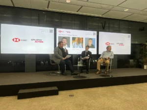 Three men sat on a stage with HSBC and Epilepsy Action logos behind them discussing the report on photosensitive epilepsy