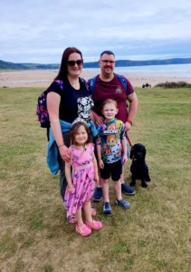 Grace and her mum, dad, brother and dog on the grass with a beach and the sea in the background