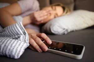 Woman waking up and turning off phone alarm. Epilepsy disrupting sleep can affect new memories forming.
