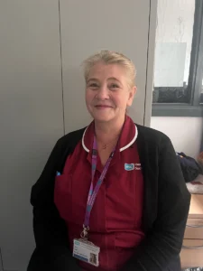 Beth irwin -nurse with blonde hair tied back and a maroon nurse uniform sitting in her office
