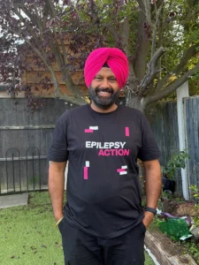 Peterborough Group Pipa Completes Epilepsy Awareness 6-Mile Walk For Epilepsy Action 2 Man stood in a garden smiling with an epilepsy action t-shirt on and a pink turban