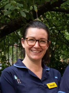 National esn hero award winner sarah clifford outside near greenery, smiling and wearing a dark blue nurse's uniform