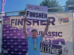 Pete holding a finisher sign and wearing a medal after completing the jurassic coast ultra marathon